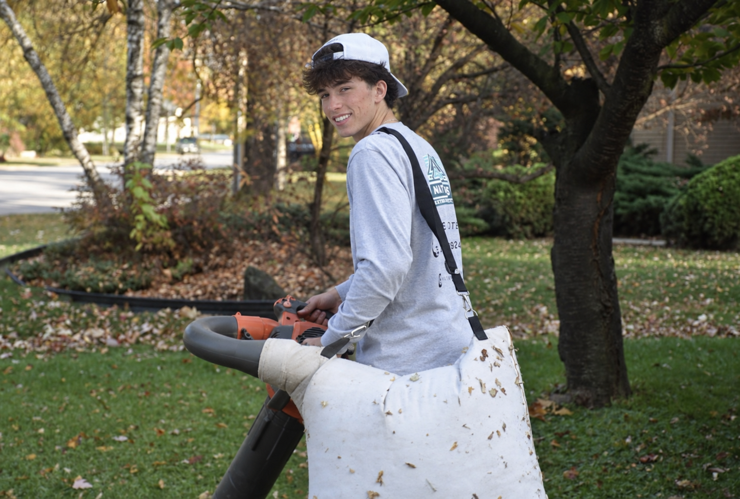 Nate smiling while clearing autumn leaves with a leaf blower in Windsor